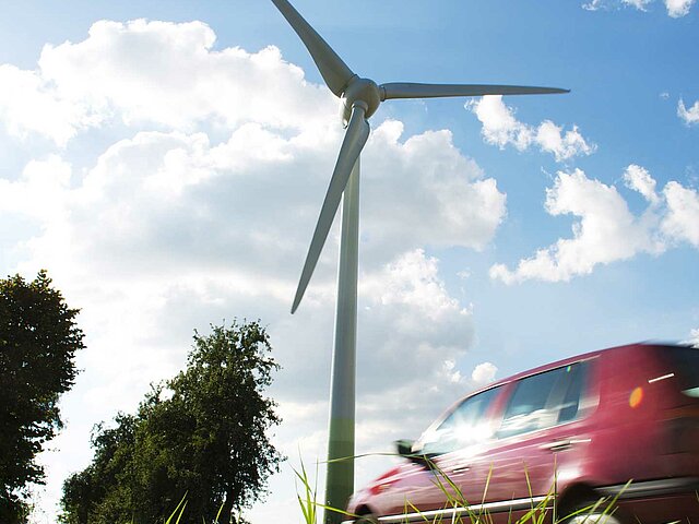 Ein Windrad ragt in den Himmel, ein Auto fährt daran vorbei