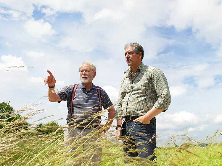 Eine Landwirt steht mit einem JUWI-Mitarbeiter auf einem Acker und deutet in die Ferne.