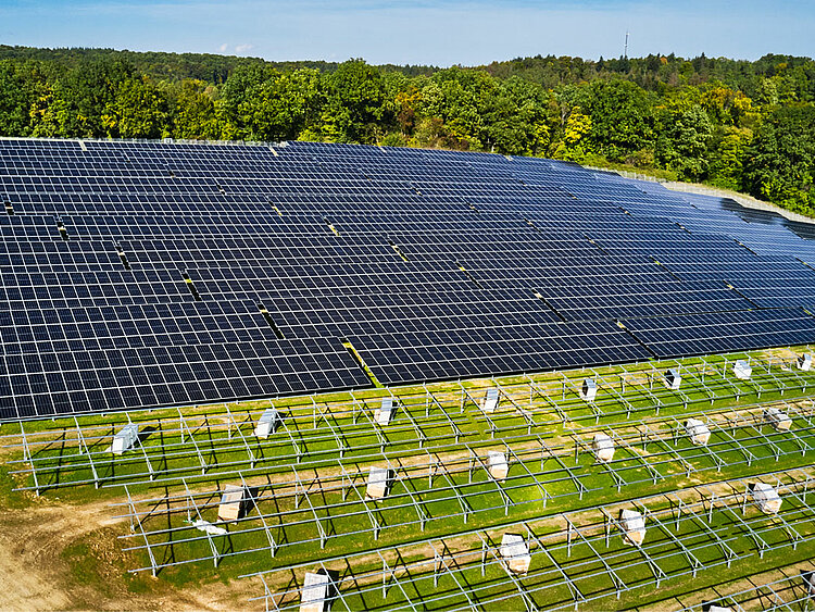 Im Hintergrund steht eine fertig aufgebaute Solar-Anlage, davor steht das Untergerüst, bereit für die Montage der Module.