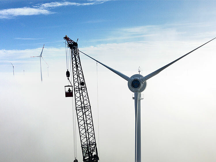 Eine alte Windenergie-Anlage reicht über die Wolken. Mit Hilfe eines Krans wird die Anlage demontiert.