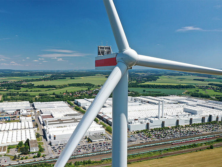 Eine Windenergie_Anlage steht vor einer großen Fabrik-
