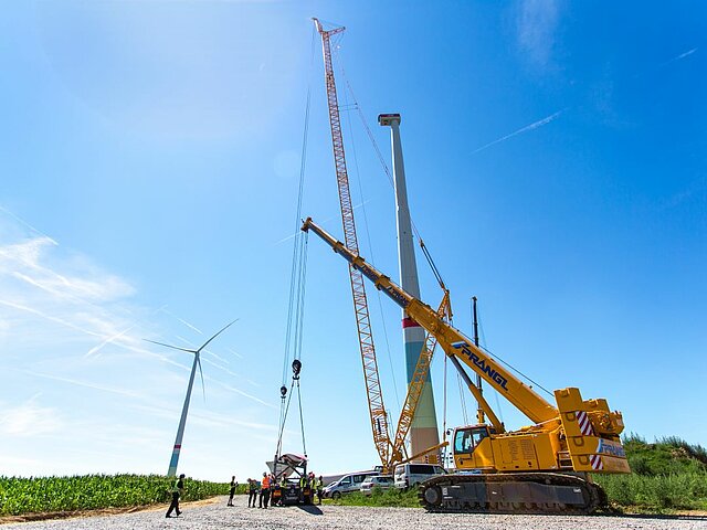 Kran zieht Rotorblatt auf eine Windenergieanlage im Offenland.