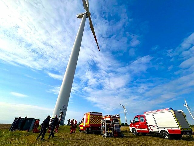 Rettungskräfte und Einsatzfahrzeuge stehen unter einem Windrad bereit für eine Höhenrettungsübung.