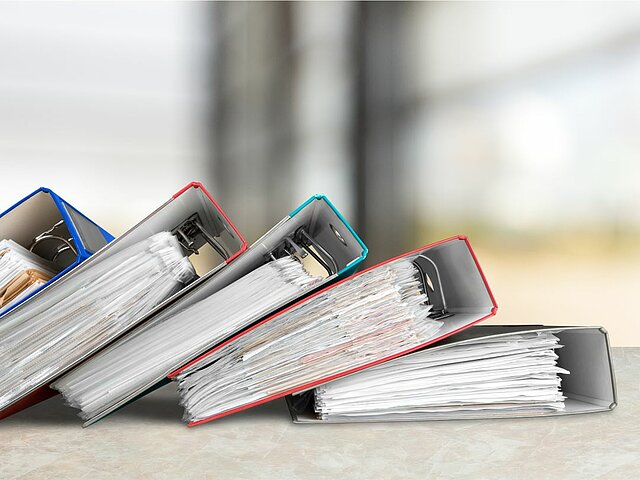 Fünf Aktenordner liegen auf einem Tisch.
