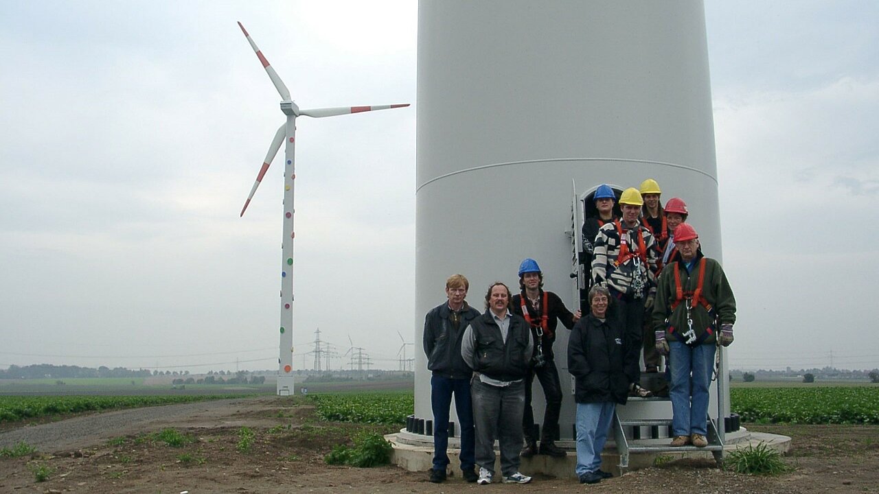 Die bunte Windenergie-Anlage erfreut sich nicht nur bei den Projektbeteiligten großer Beliebtheit. Eine Gruppe von Menschen posiert vor der "Smarties Mühle".