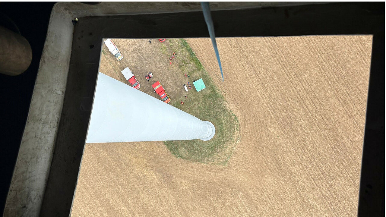 Der Windpark Herrnsheim liegt in Rheinland-Pfalz nahe Worms. An der Übung beteiligten sich Vertreter aller betroffenen Gemeinden sowie angrenzender Stadtgebiete. Perspektive aus der Kranluke einer Windenergieanlage auf ein Feld mit Rettungsfahrzeugen hinab.