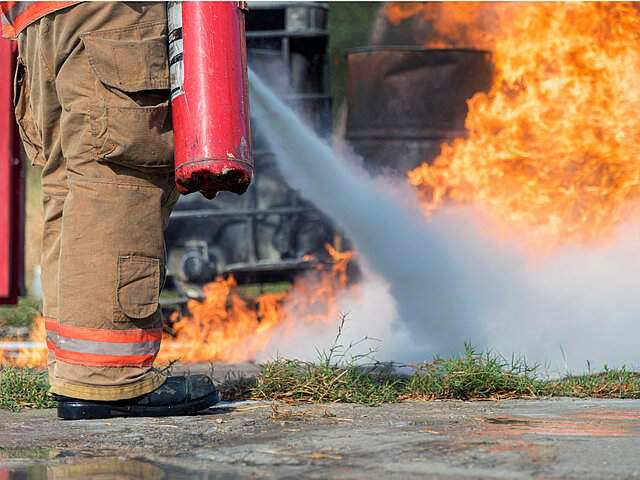 Feuerwehrmann löscht Bodenbrand mit hohen Flammen mit einem Feuerlöscher.