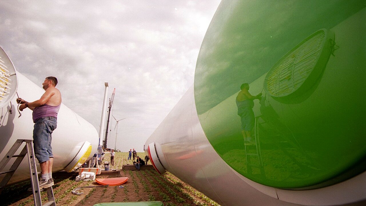 Die Leuchtfelder bestehen aus Plexiglas und Neonröhren und verteilen sich über die Länge des Turms. Ein Handwerker installiert die leuchtenden Punkte an den Bestandteilen der Windenergieanlage.
