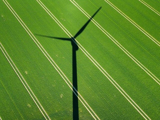 Der Schatten einer Windenergieanlage auf einer grünen Wiese.