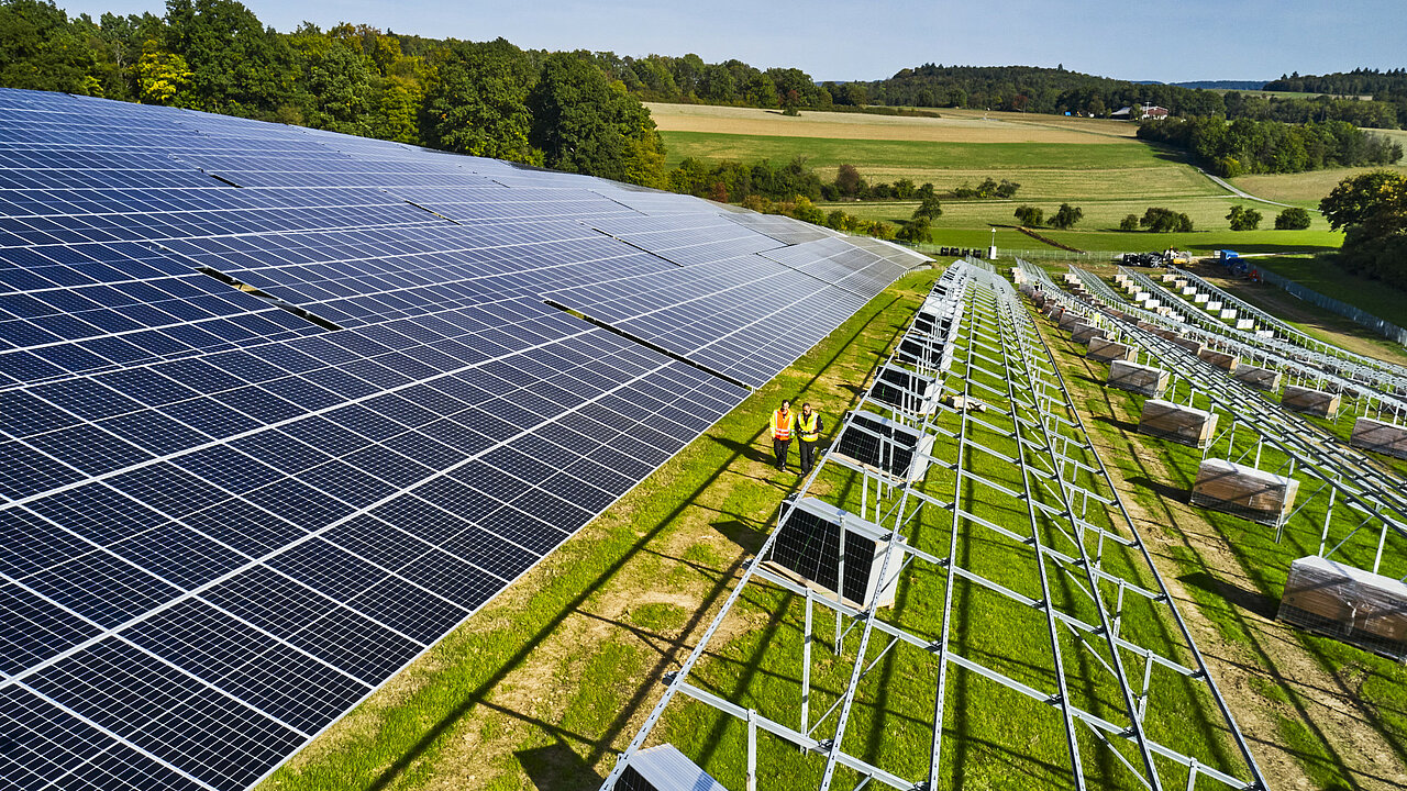 Die Pflege von Solarparks in Hanglagen bringt besondere Herausforderungen mit sich. In Seckach etwa beträgt die Hangneigung bis zu 20 %. Solche Steillagen erfordern spezialisierte Mähgeräte oder sogar manuelle Maßnahmen, um Erosion zu vermeiden und die Arbeitssicherheit zu gewährleisten. Hinzu kommen wirtschaftliche Zwänge, die häufig zu geringeren Reihenabständen führen. In Seckach sind die Fahrgassen weniger als drei Meter breit – das erschwert den Einsatz von Maschinen erheblich. Zusätzlich behindern zahlreiche Verstrebungen an den Modultischen die Pflegearbeiten. Der steinige Boden stellt eine weitere Herausforderung dar. Auf einer Fläche von 14 Hektar müssen hier alle Maßnahmen besonders sorgfältig geplant und umgesetzt werden, um einen sicheren und effizienten Betrieb zu gewährleisten. Freiflächensolarpark am Hang gebaut mit noch teils fehlenden Modulen.