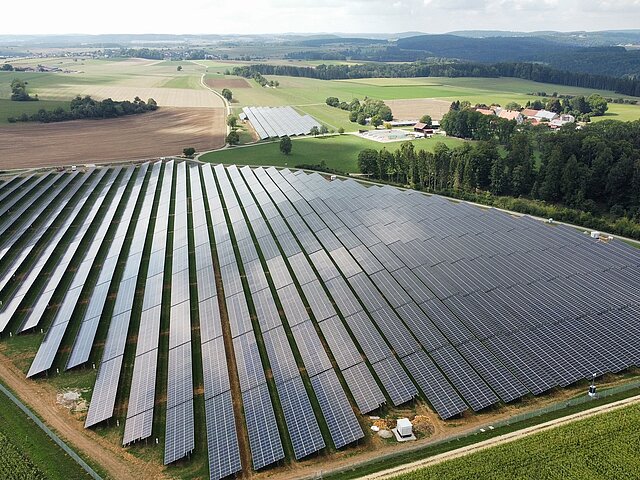 Ein PV-Park auf offener Fälche. Im Hintergrund erheben sich Berge. 